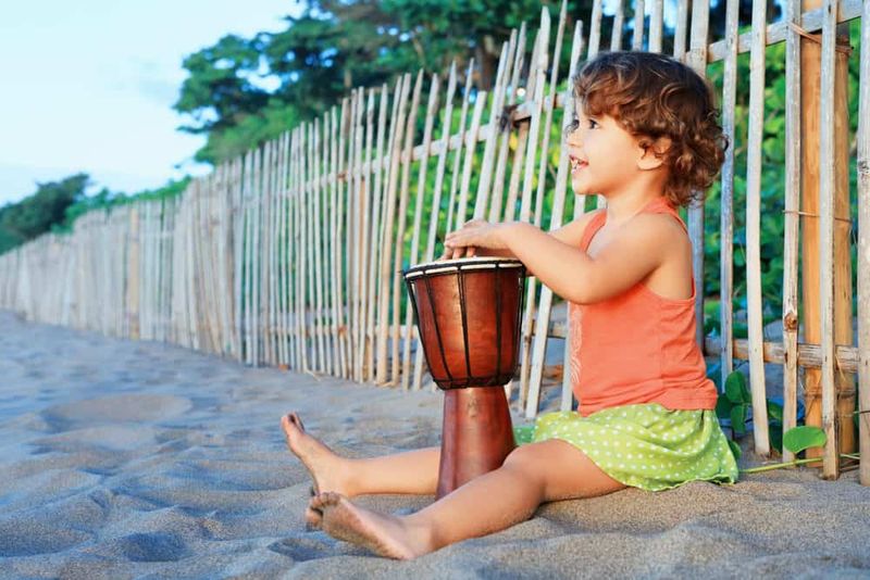 Gadis kecil yang bahagia memainkan djembe drum tangan afrika tradisional